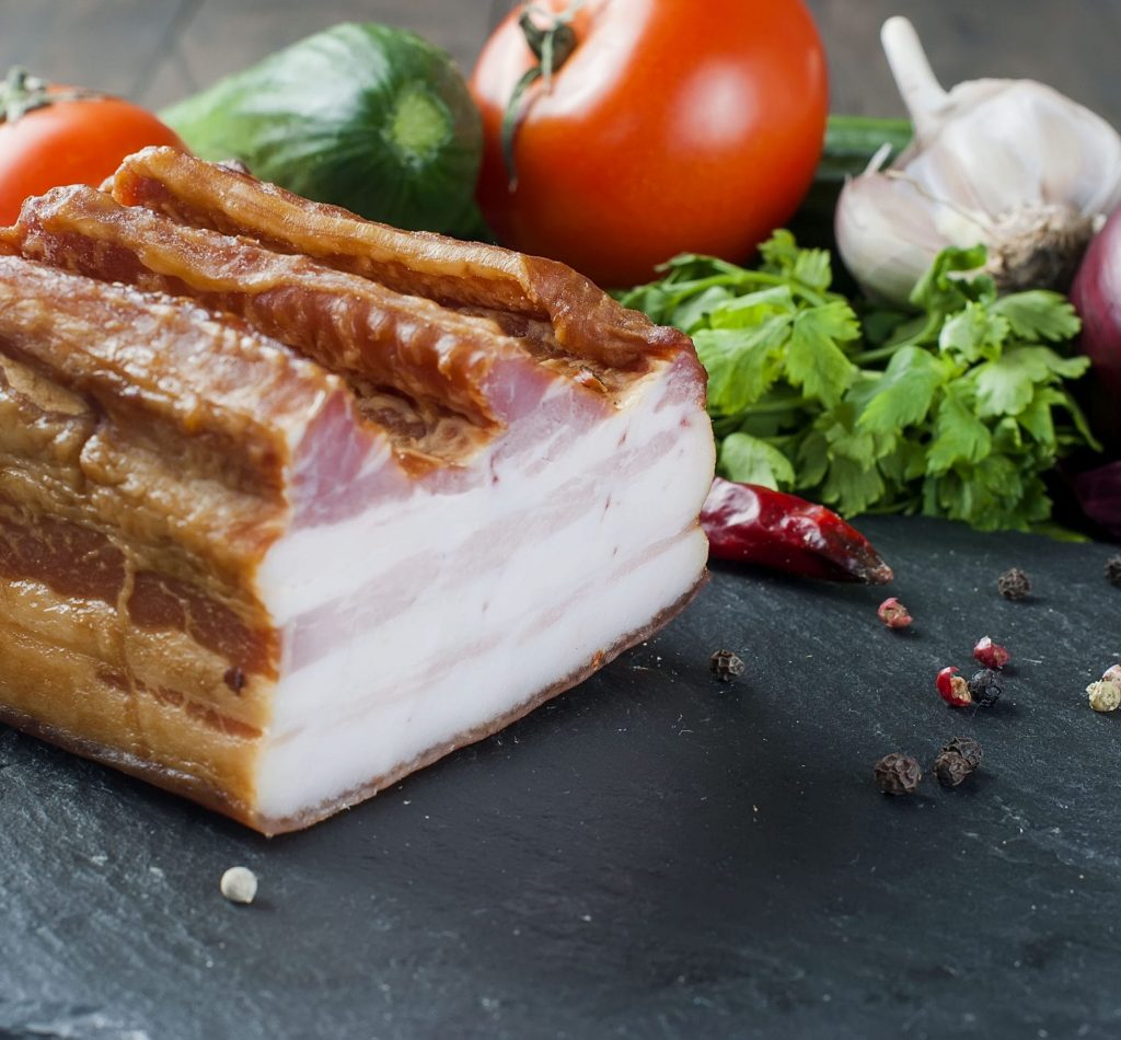 Smoked bacon with vegetables on stone black board